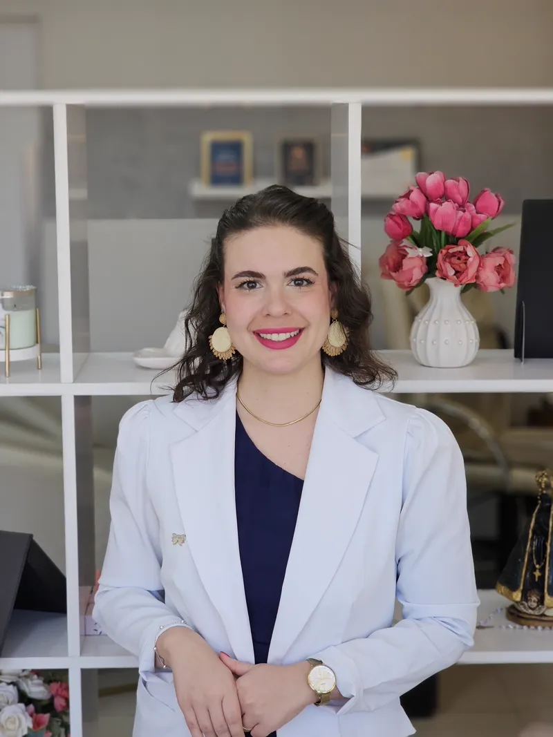 Dra. Paula Rode Caliani, biomédica esteta, sorrindo em seu consultório, vestindo jaleco branco.